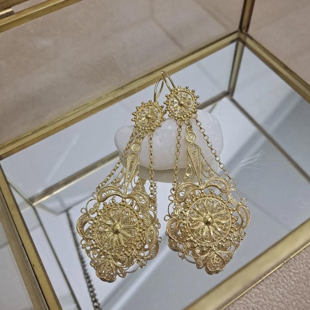 Par de brincos de filigrana em ouro, pousados sobre uma caixa de vidro e latão