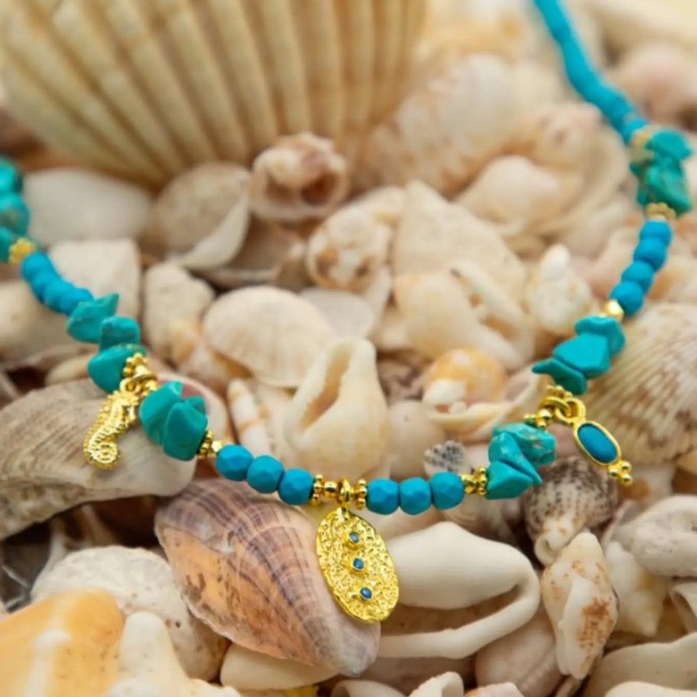 Pulseira com contas de turquesa e apliques dourados, pousada sobre conchas