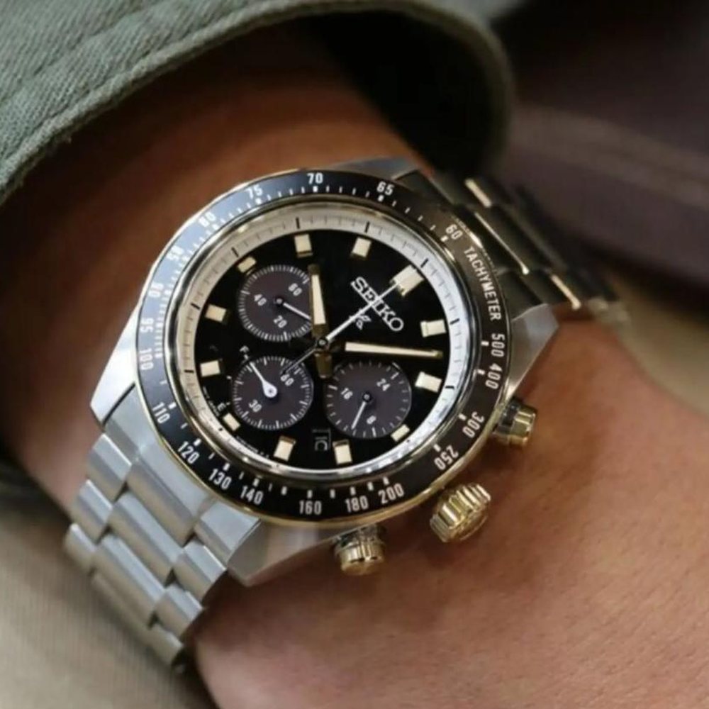 Relógio cronógrafo Seiko em aço, com mostrador preto e coroa dourada, usado no pulso